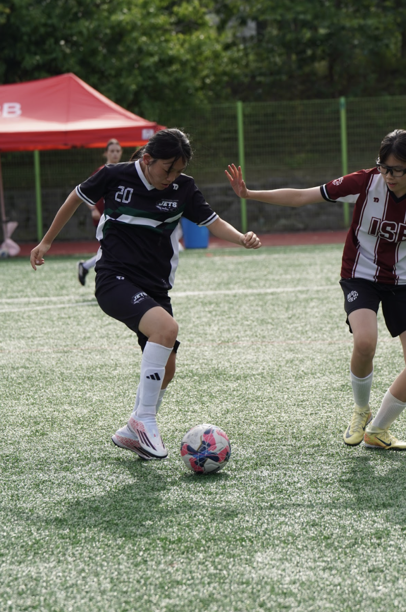 Striker Mary Cho (20) dribbles toward the goal while facing an ISB defender and searching for space to advance the attack. Maintaining close control under pressure, she works to create an opening in the final third.
